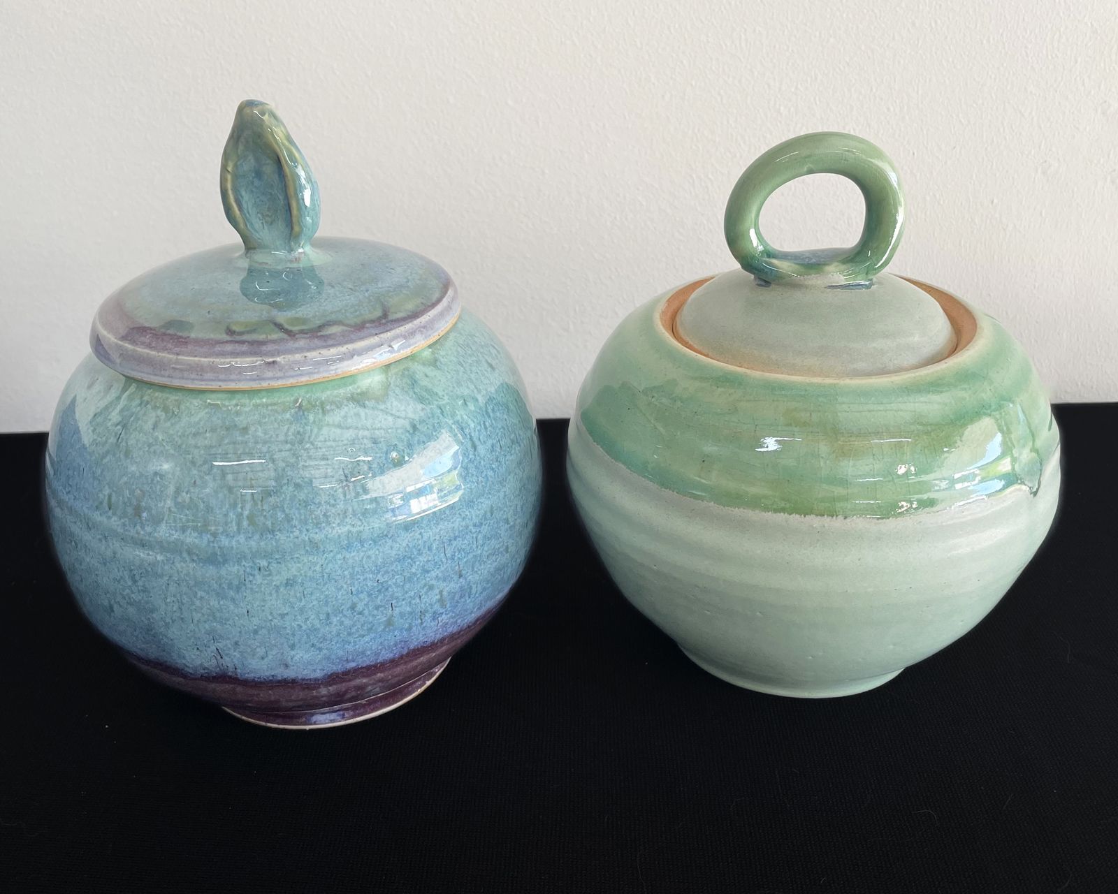 Two handmade lidded ceramic vessels in river-inspired blue and green glazes.